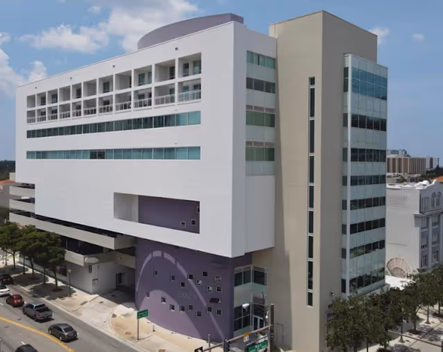 Modern multi-story building exterior with a purple entrance, viewed from the street.