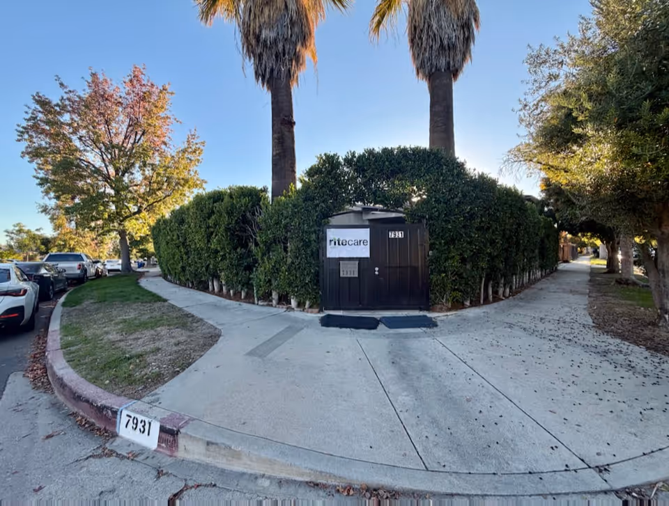 A gated hedge surrounds a small front entrance with a RiteCare sign and palm trees.