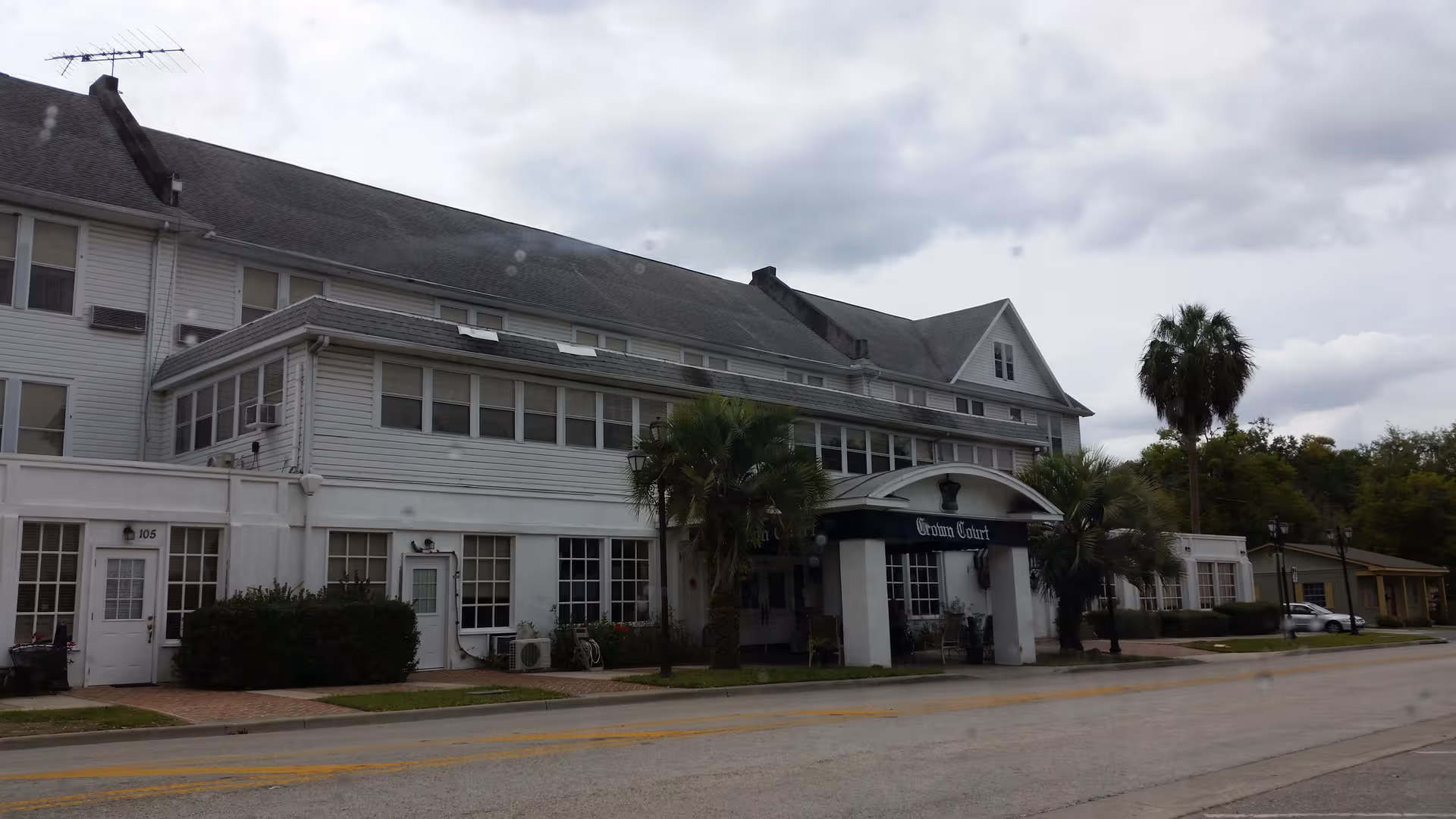 Two-story white senior living facility with Crown Court entrance and palm trees along a street.