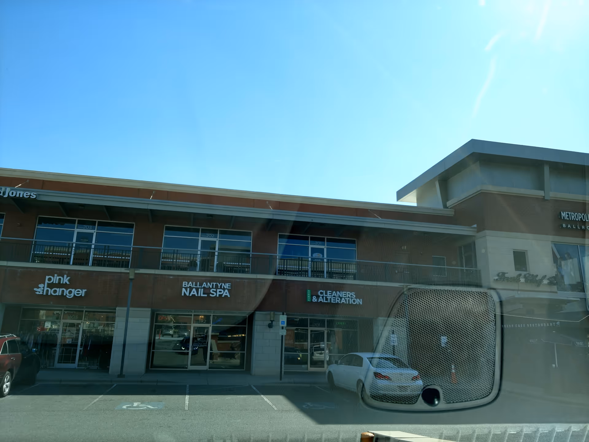 Facade of a strip mall with nail spa, cleaners, and storefronts under a blue sky.