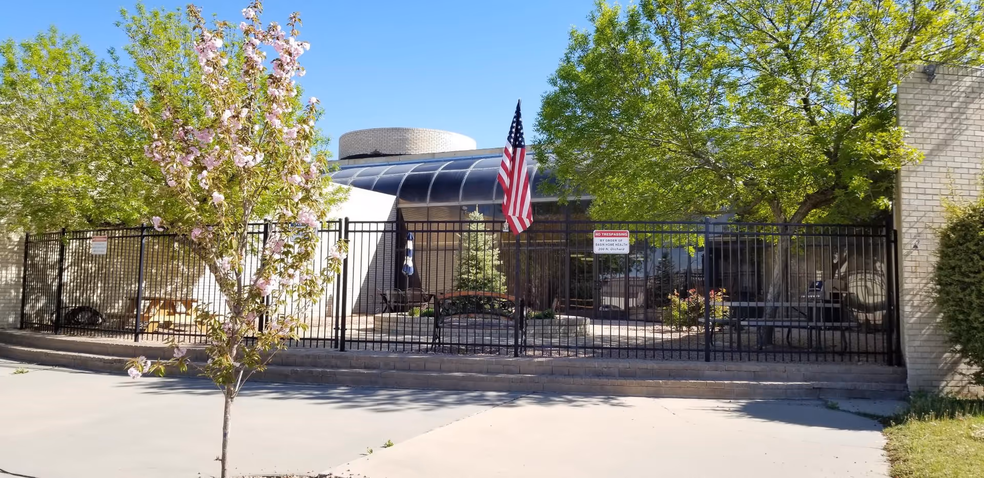 Exterior view of Basin Home Health and Hospice facility with gate, trees, and American flag