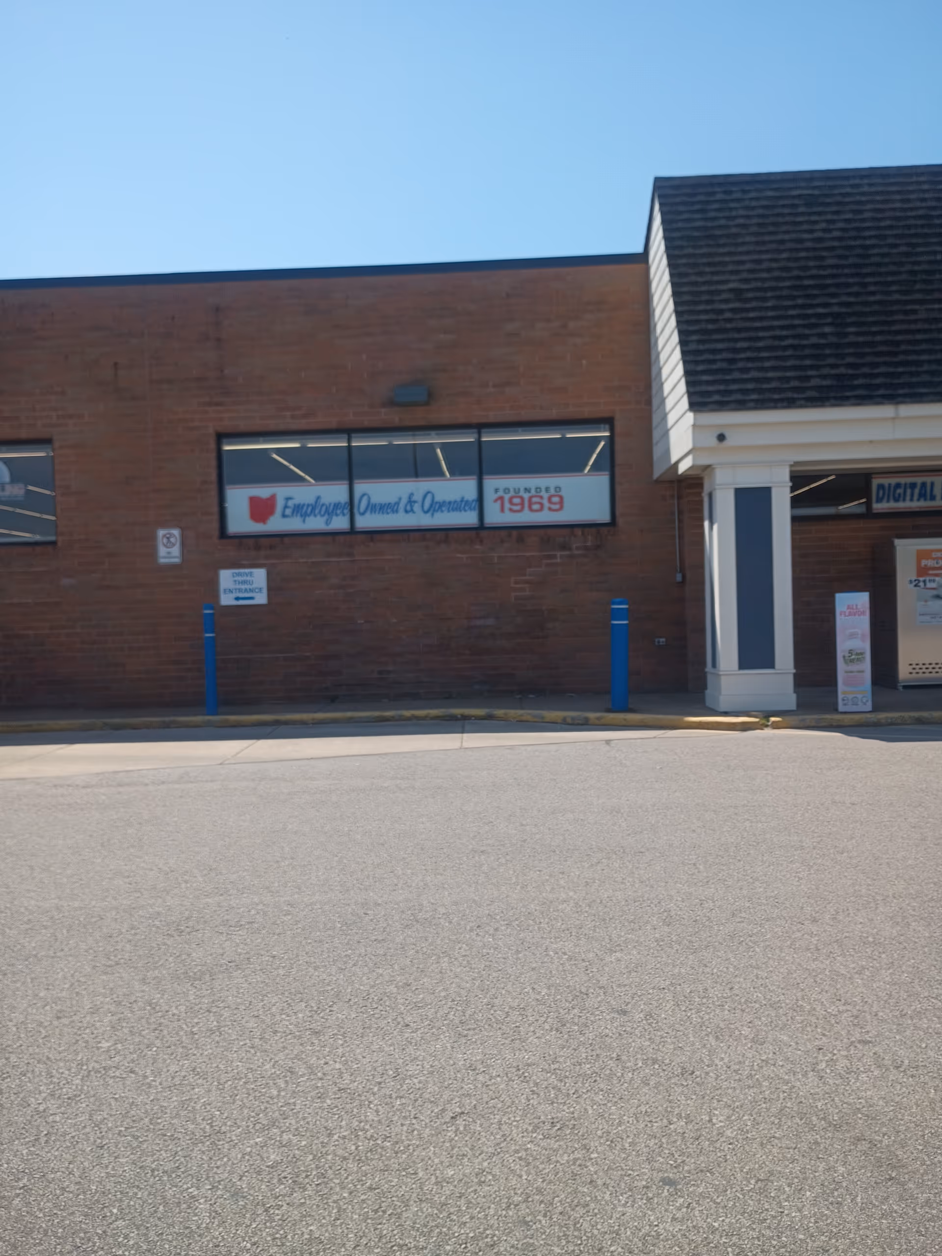 Exterior view of Discount Drug Mart storefront with brick facade and blue bollards.