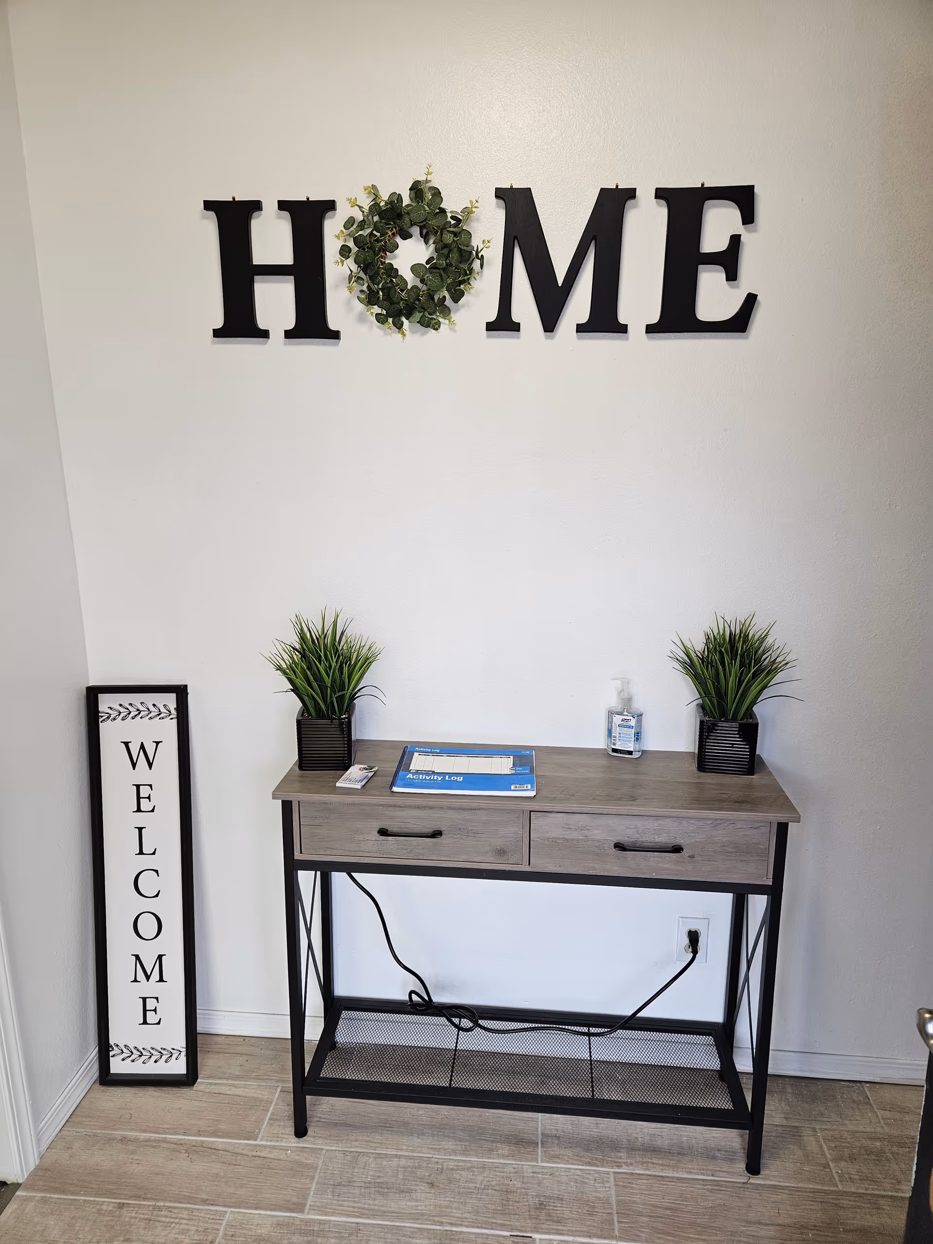 Interior entryway with a console table, two plants, and a large 'HOME' sign.