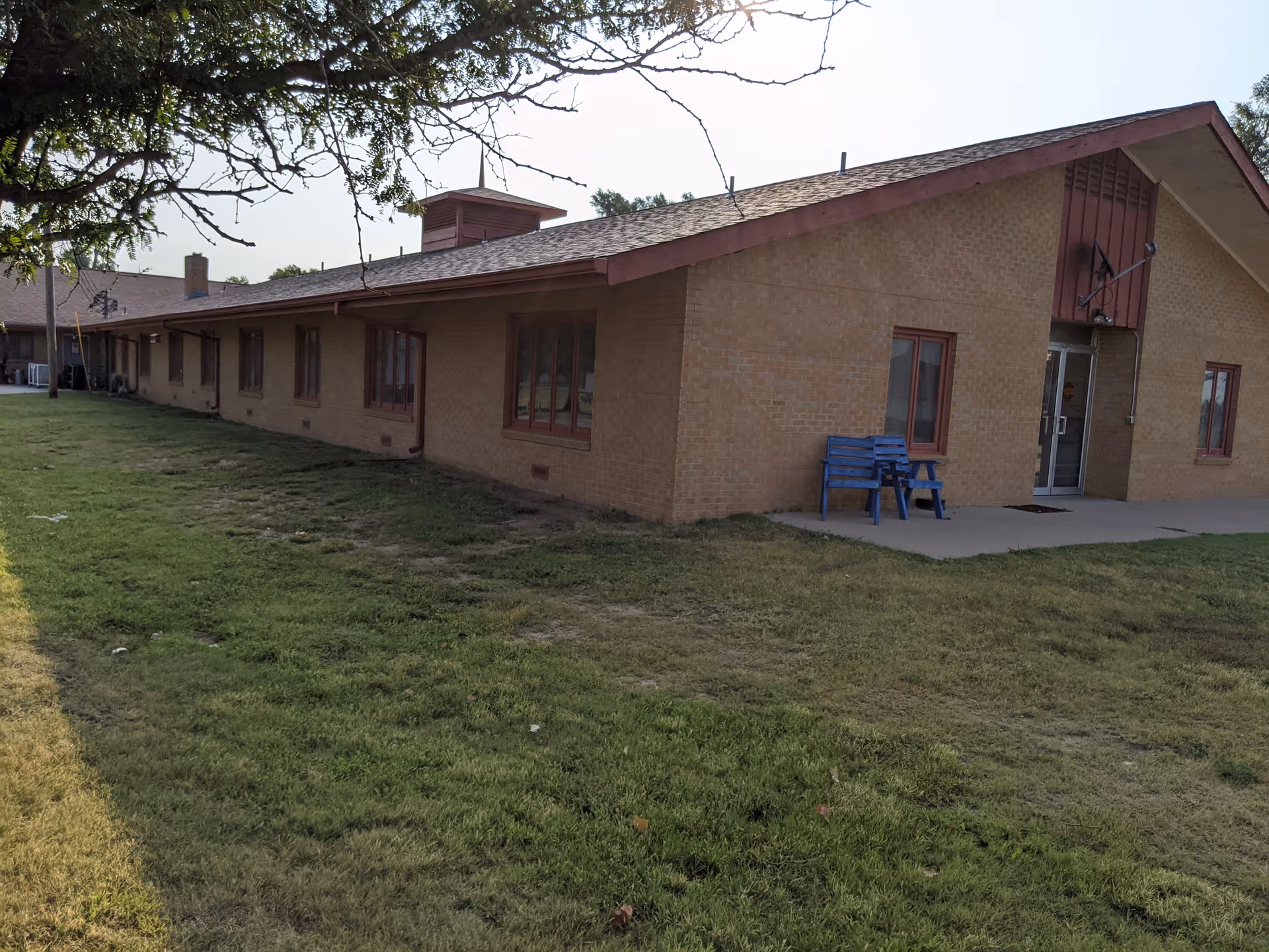 Single-story brick senior living building with a blue bench by the entrance and grassy lawn.