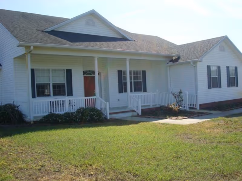 White single-story senior living facility with a front porch and green lawn