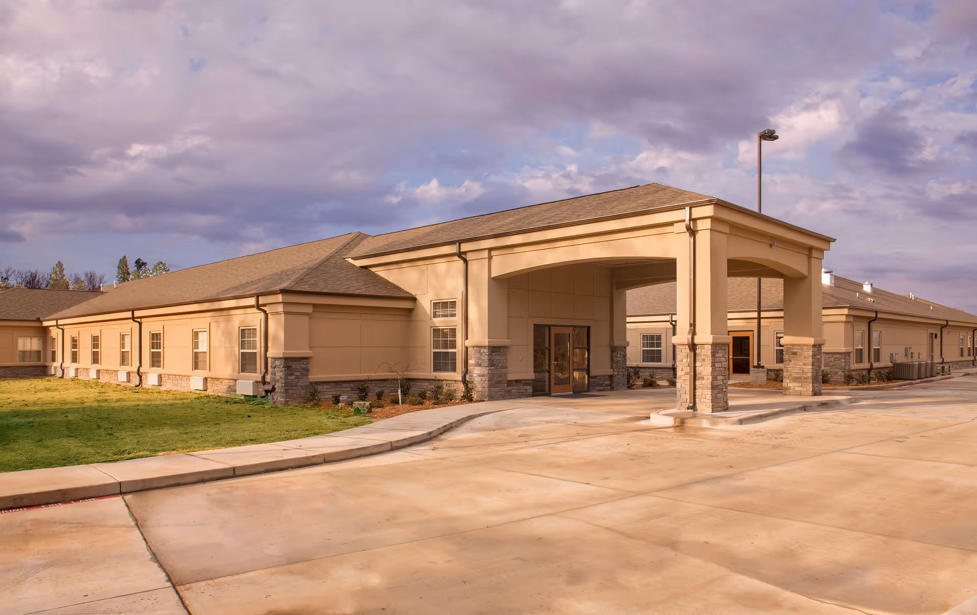 Exterior view of a beige senior care facility with a covered entrance and stone columns.