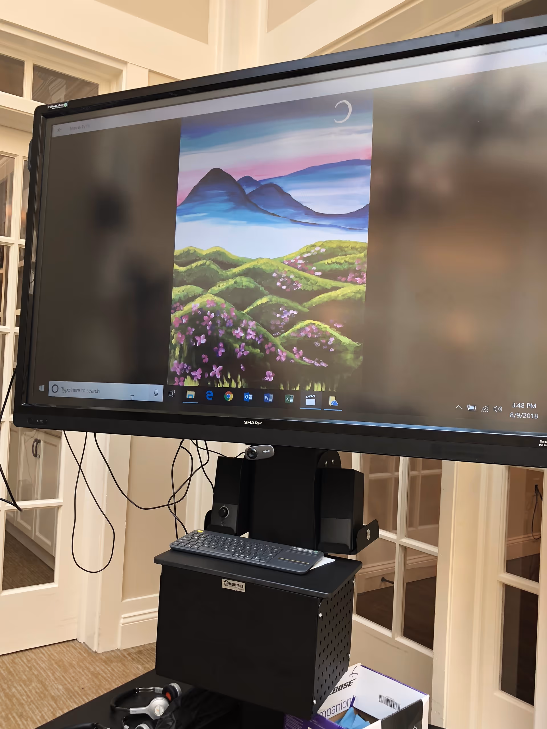 A large monitor on a black mobile stand displays a mountain landscape wallpaper.