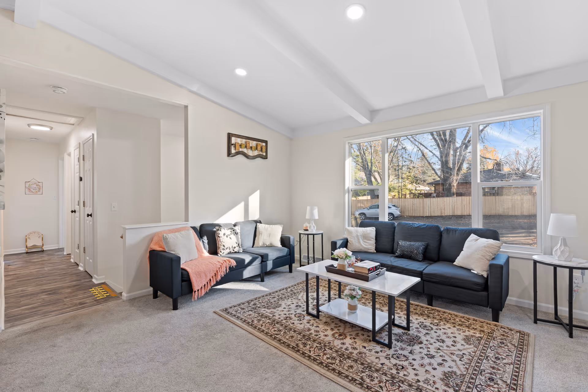 Sunlit senior living room with navy sofas, coffee table, rug, and large windows.