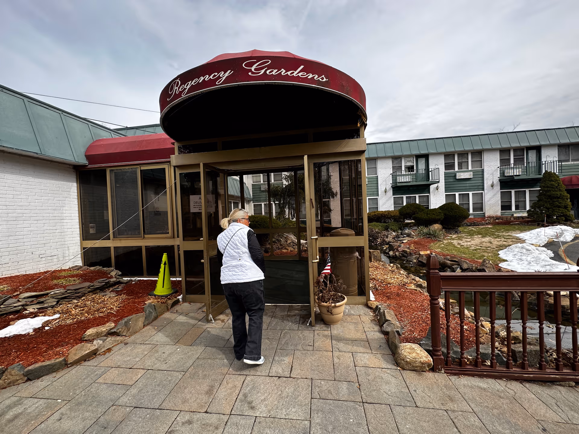 Person entering glass doors under a red curved canopy labeled Regency Gardens at an exterior facility.