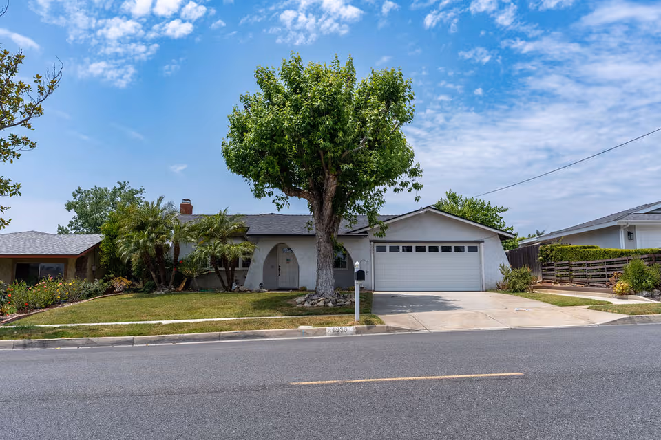 Front view of Genesis Manor VI, a single-story residence with a large tree and driveway.