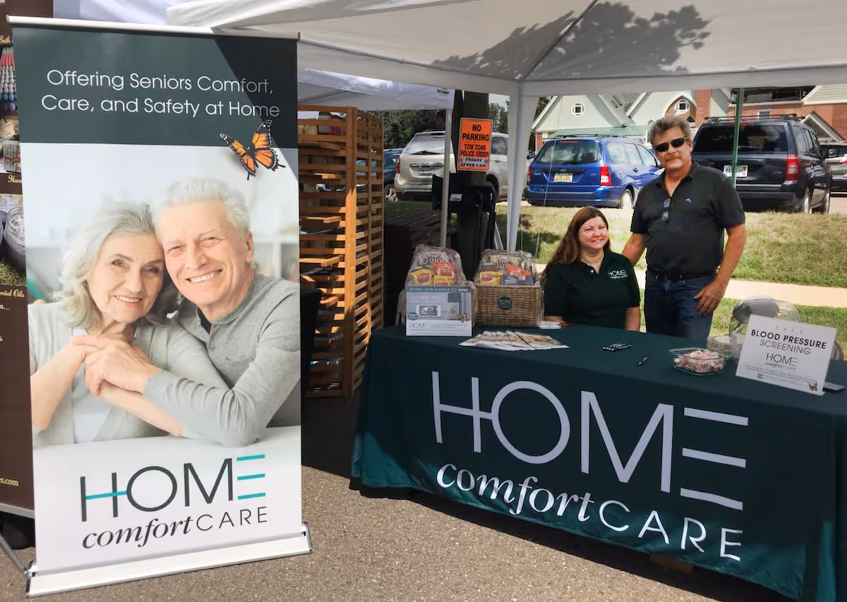 Outdoor booth for Home Comfort Care with a large banner and two staff at a table.