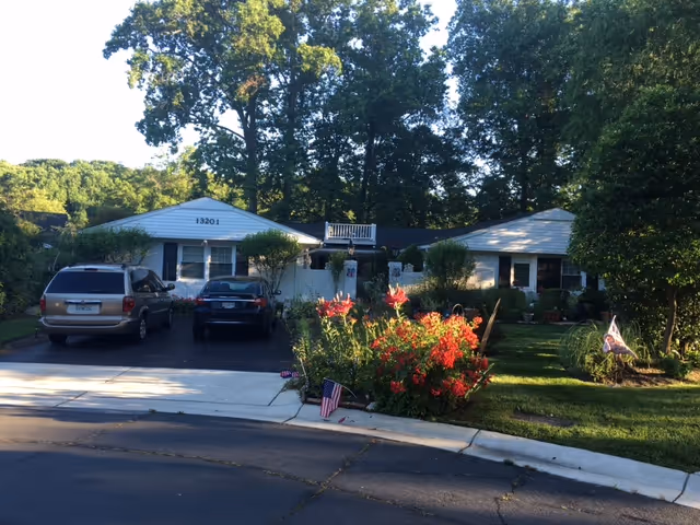 Front exterior of a single-story assisted living home with cars in the driveway and colorful flowers.