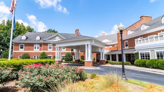 Brick senior living facility with a covered entrance, flagpole, and manicured landscaping.