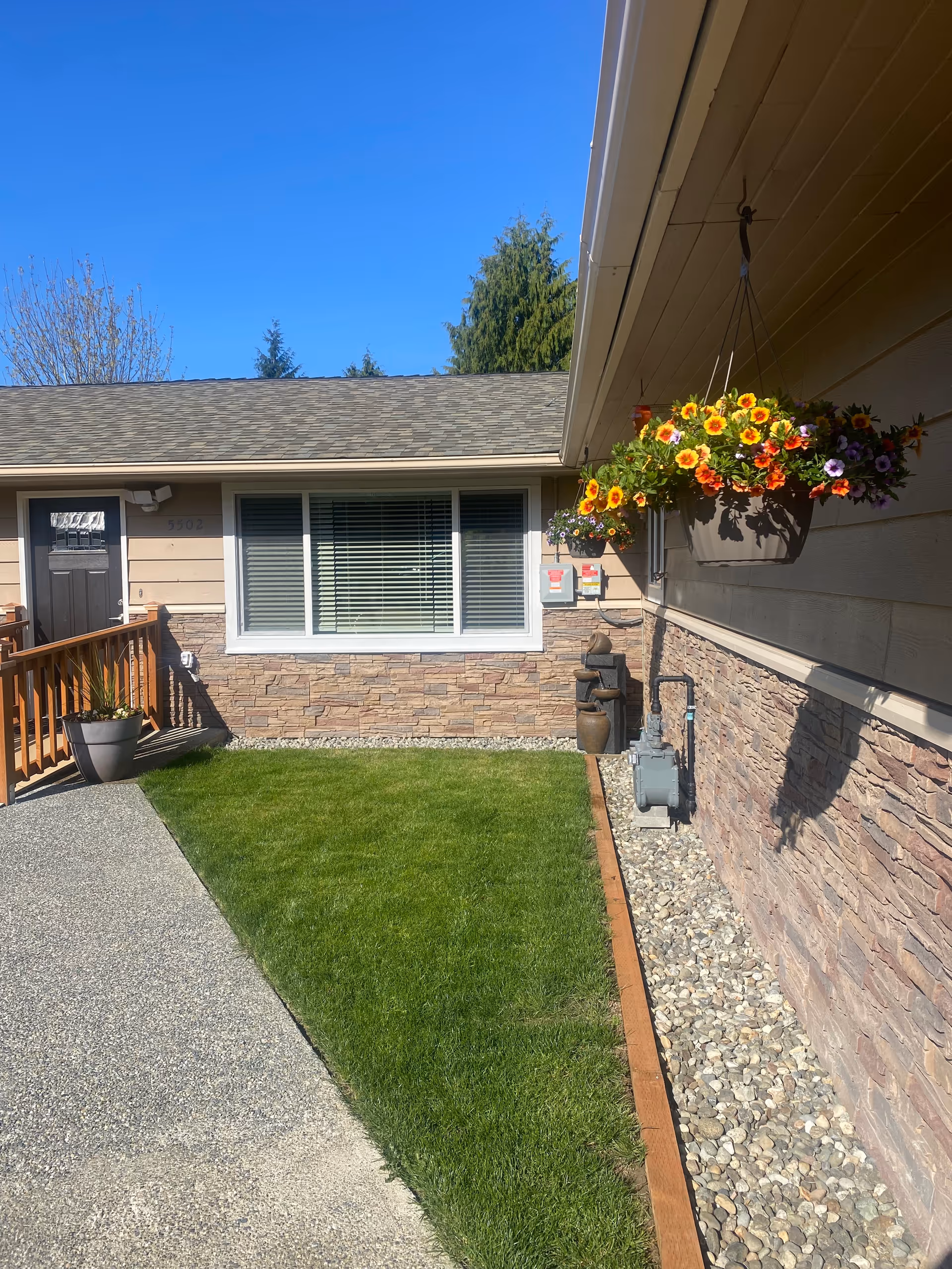 Exterior view of a single-story senior care home with a front window, hanging flowers, and lawn.