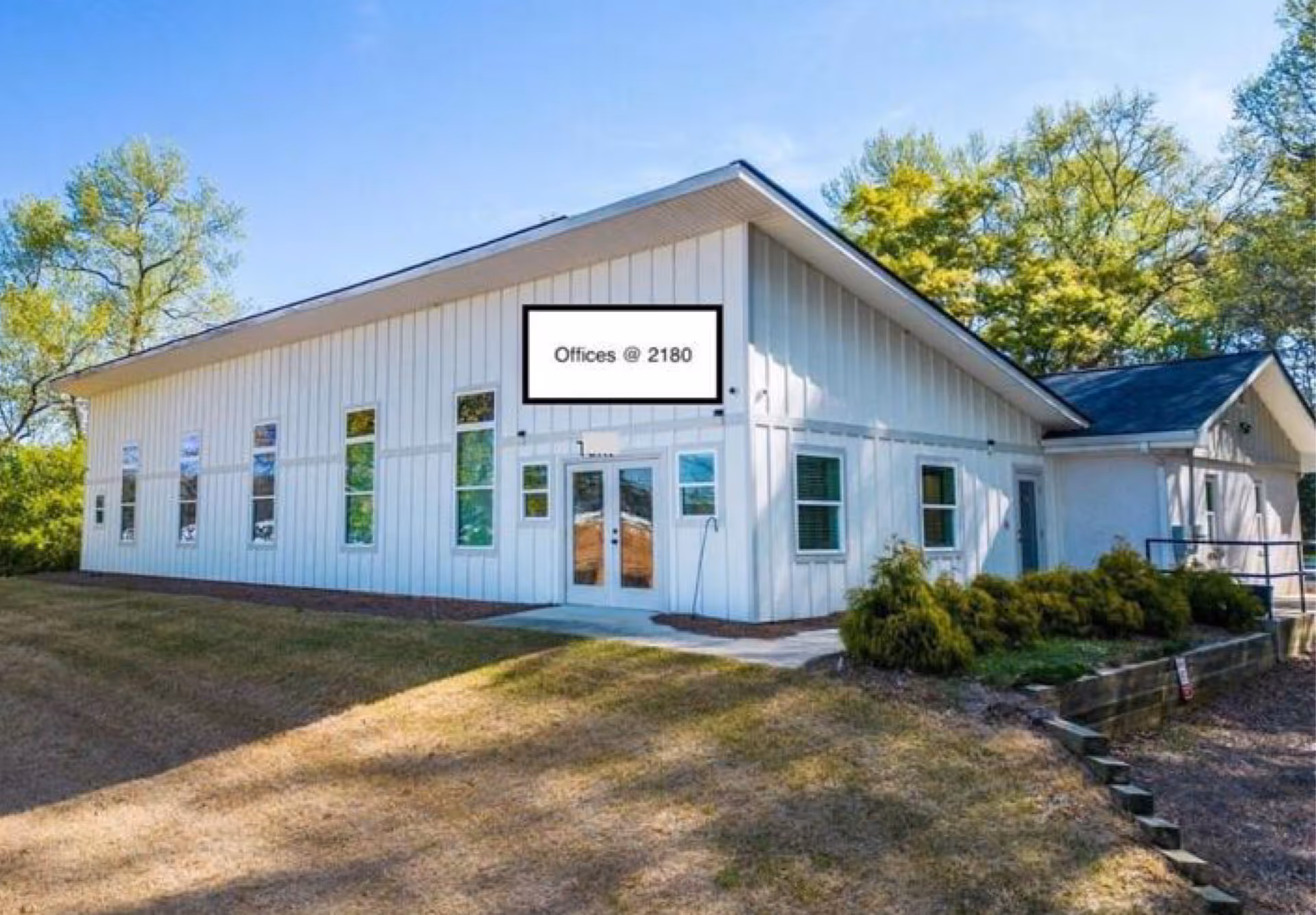 White exterior building with multiple windows and a sign: Offices @ 2180.