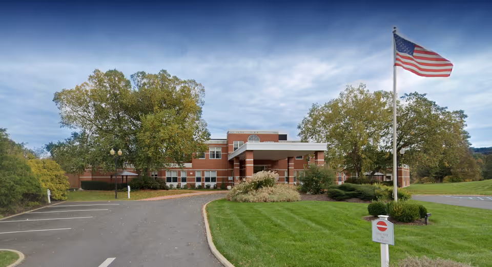 Exterior view of Wingate at Ulster senior living facility with flag and manicured lawn.