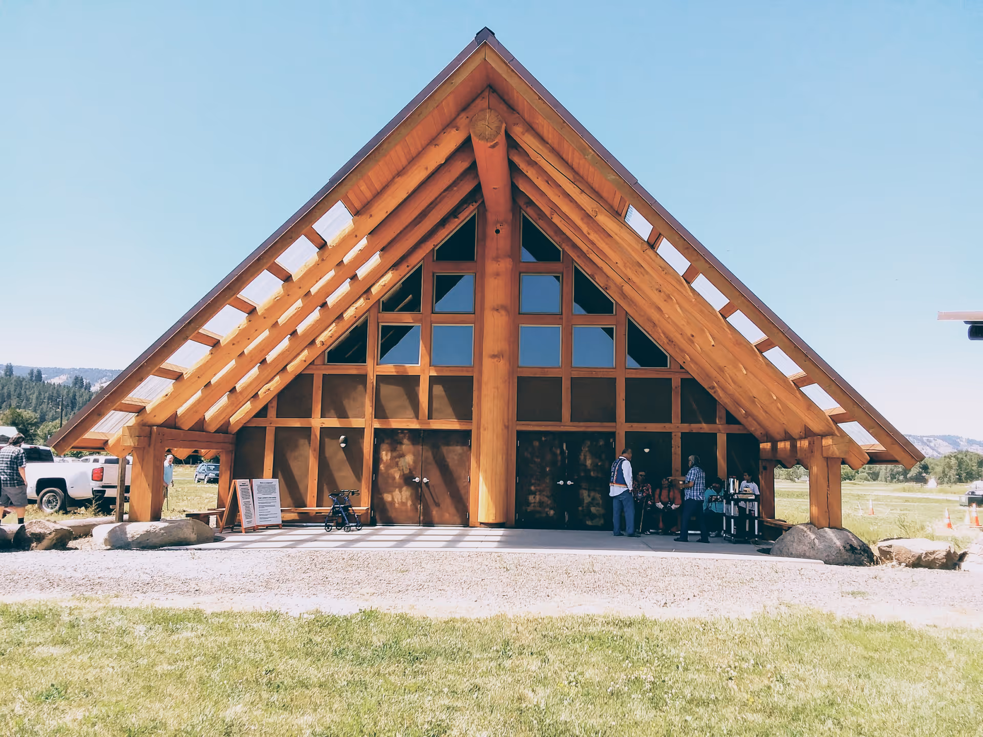 A large wooden A-frame building exterior with glass windows and people at the entrance.