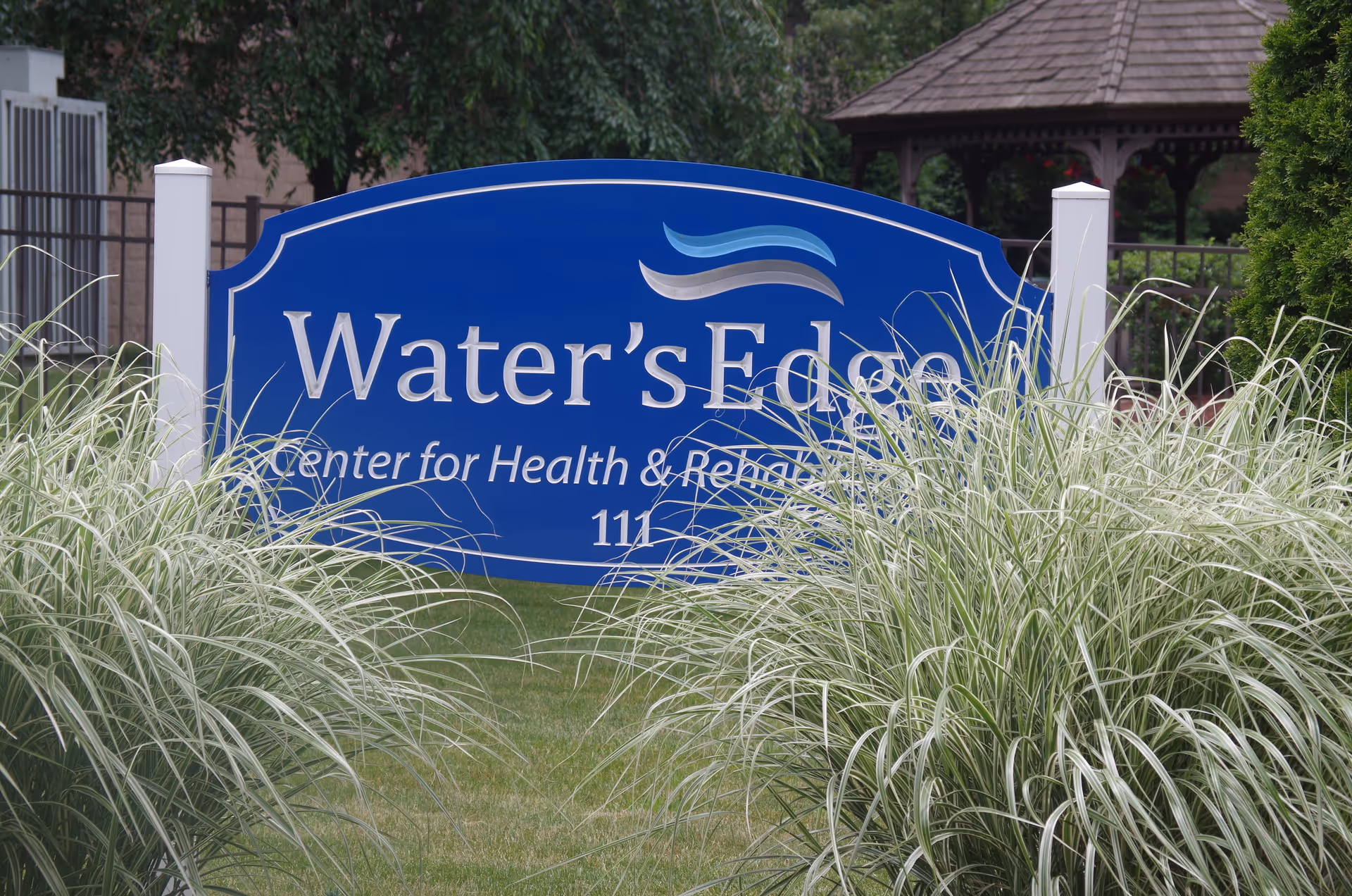 Blue Water's Edge sign reads Water's Edge Center for Health & Rehabilitation, surrounded by tall grasses.