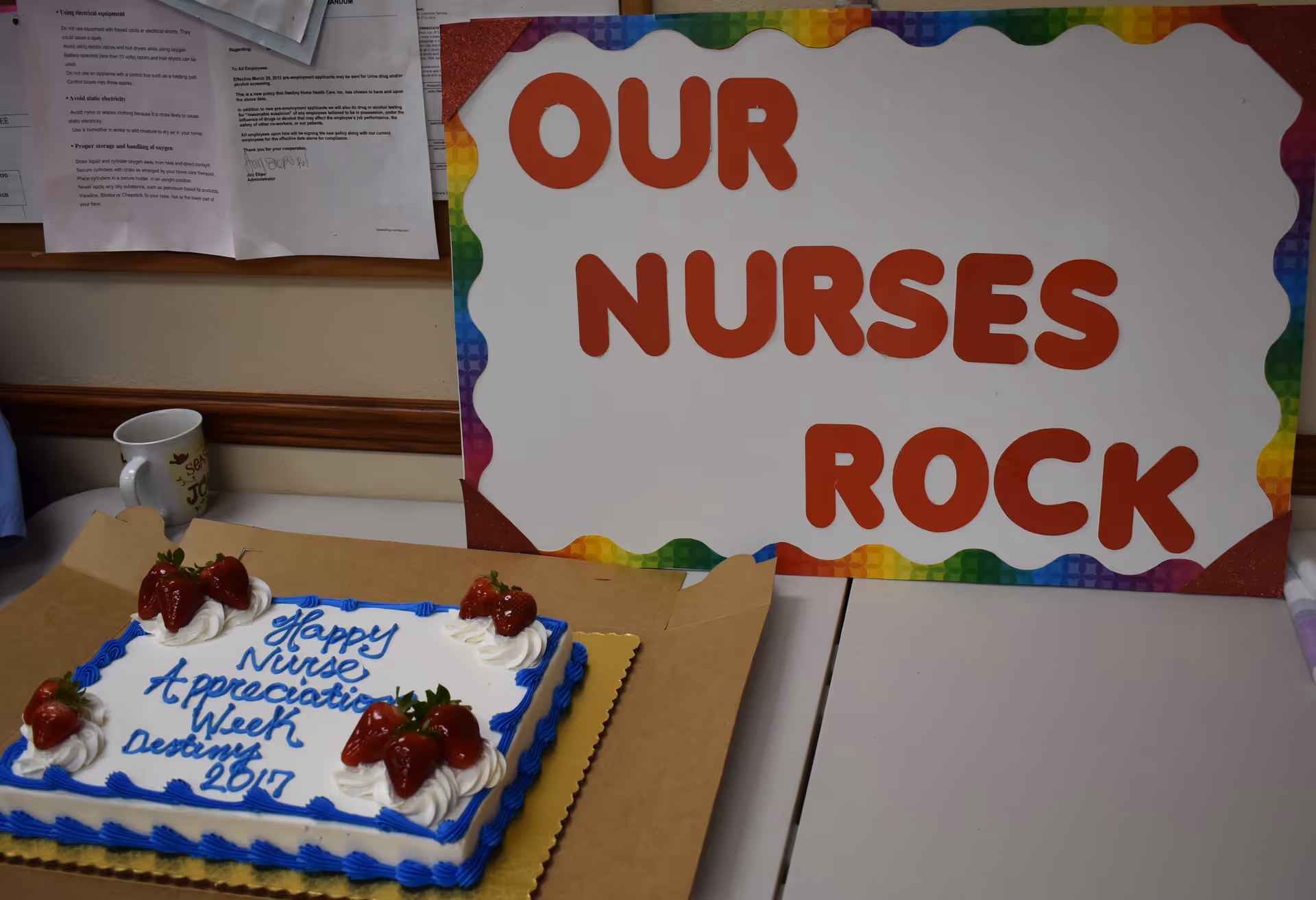 Colorful sign reading Our Nurses Rock beside a decorated cake on a table indoors.