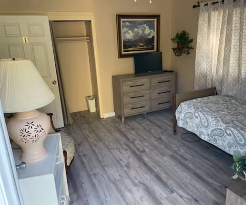A cozy bedroom in a senior living unit with a bed, dresser, TV, and closet.
