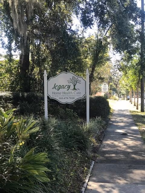 A Legacy Home Health Care sign on a landscaped lawn beside a sidewalk.