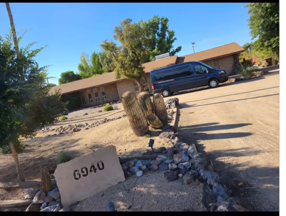 Single-story brick facility with a blue van parked beside a desert landscape and rocks.