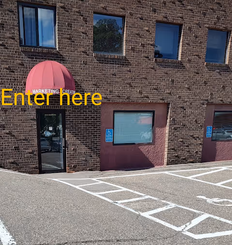 Brick building exterior with a pink curved awning over the entrance and marked parking spaces.