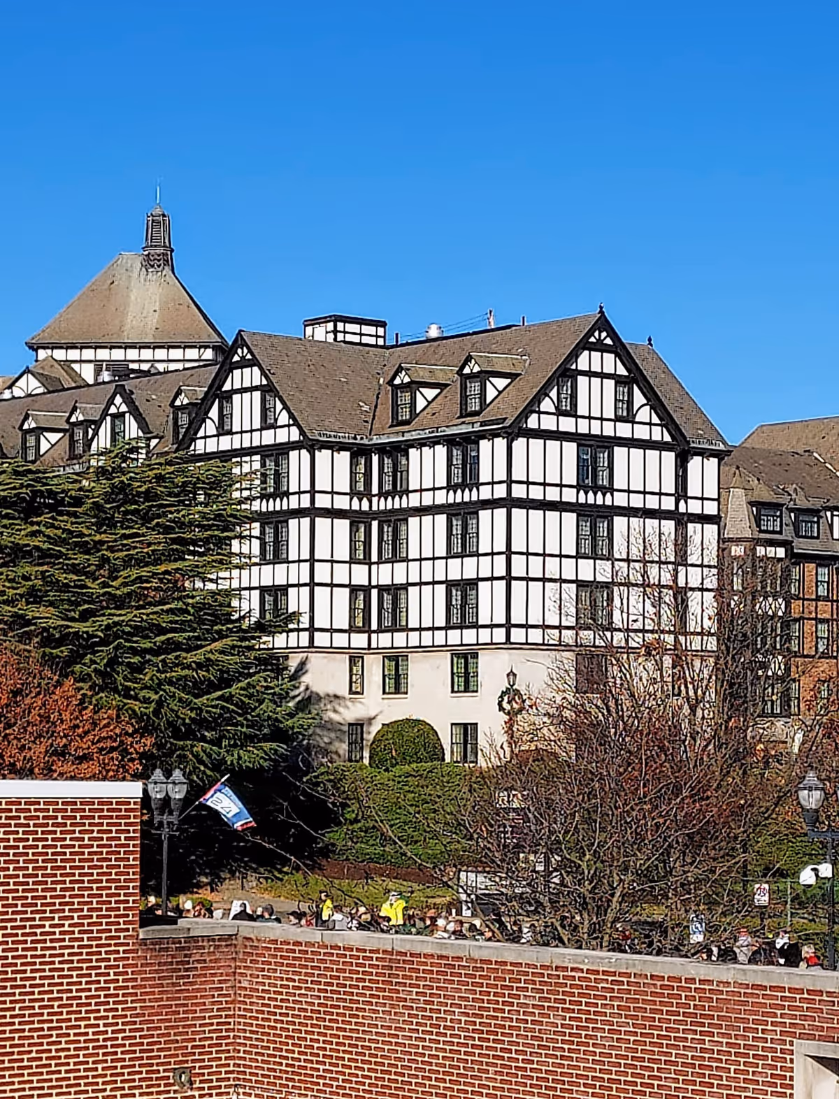 A Tudor-style senior living building with a brick foreground and people along an outdoor walkway.