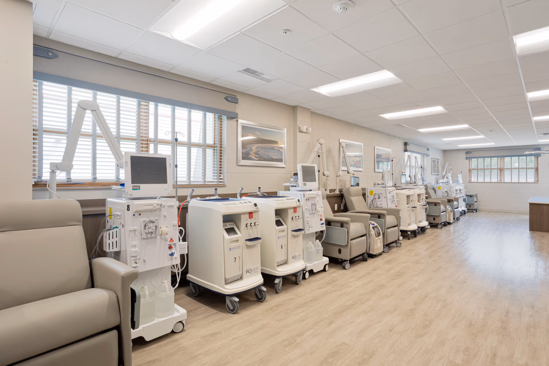 Row of medical dialysis chairs and machines inside a well-lit patient treatment room.