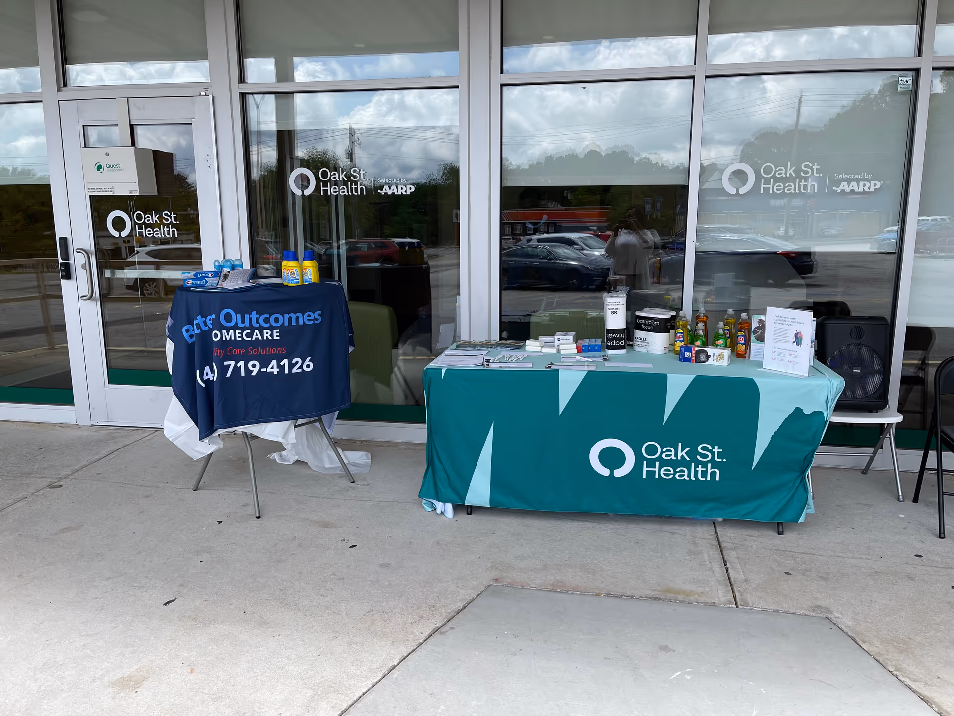 Two promotional tables with Oak St. Health banners sit outside the Better Outcomes Home Care facility.