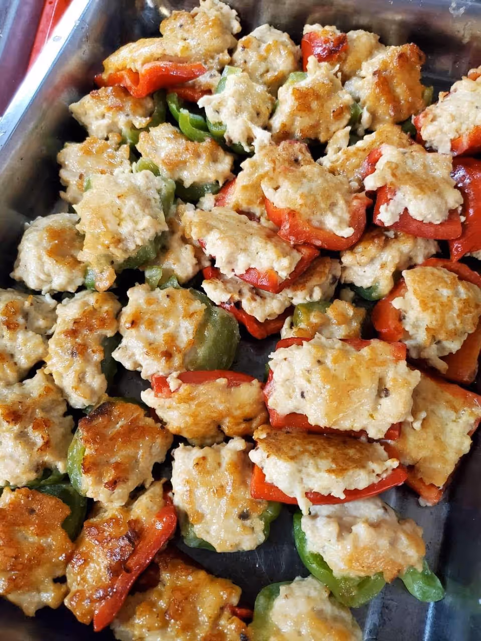 A tray filled with cooked stuffed bell peppers, both red and green, topped with a browned mixture that appears to be a meat or cheese filling.