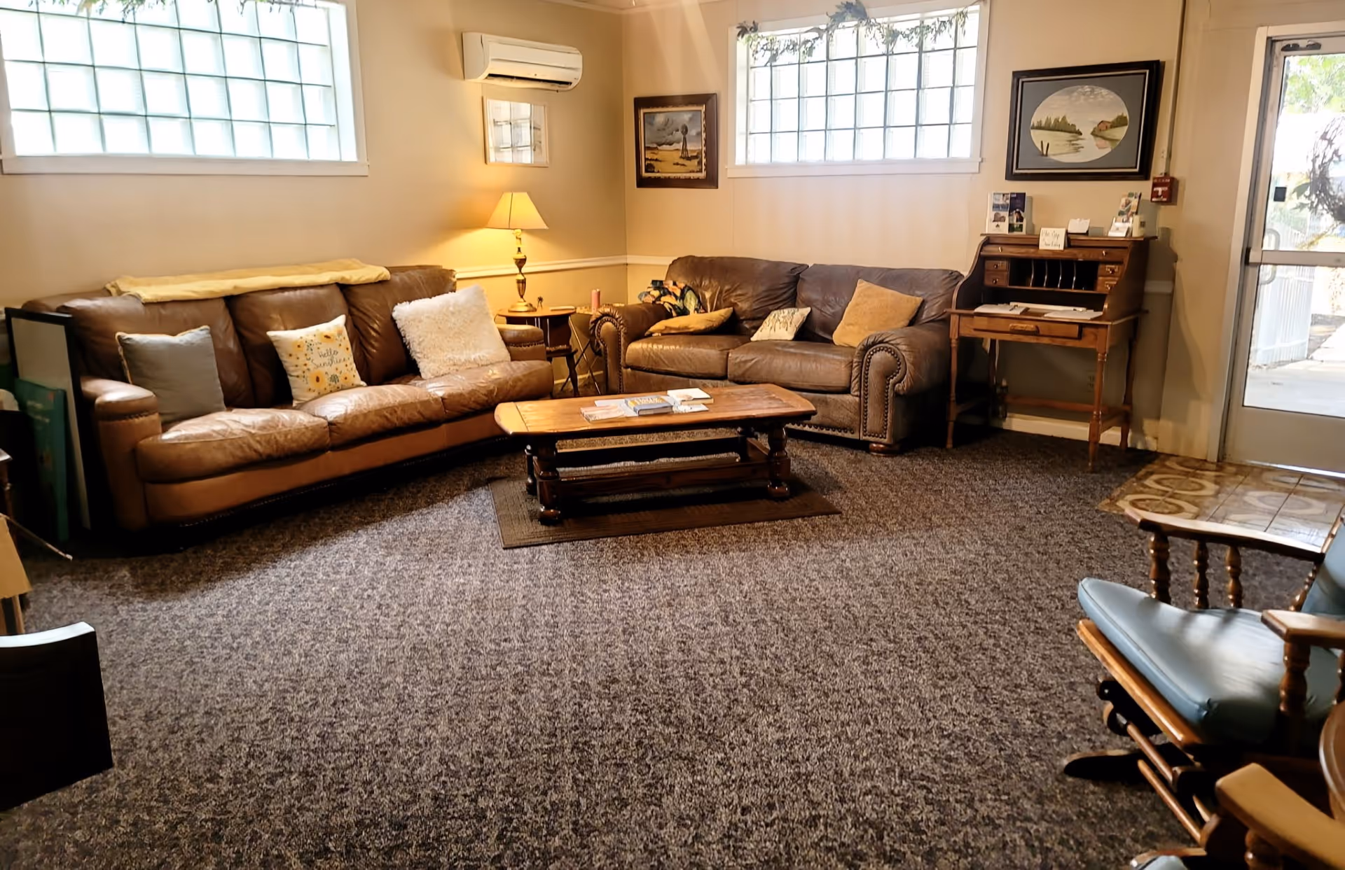 Cozy living room in a senior living facility featuring brown leather couches, coffee table, and lamps.