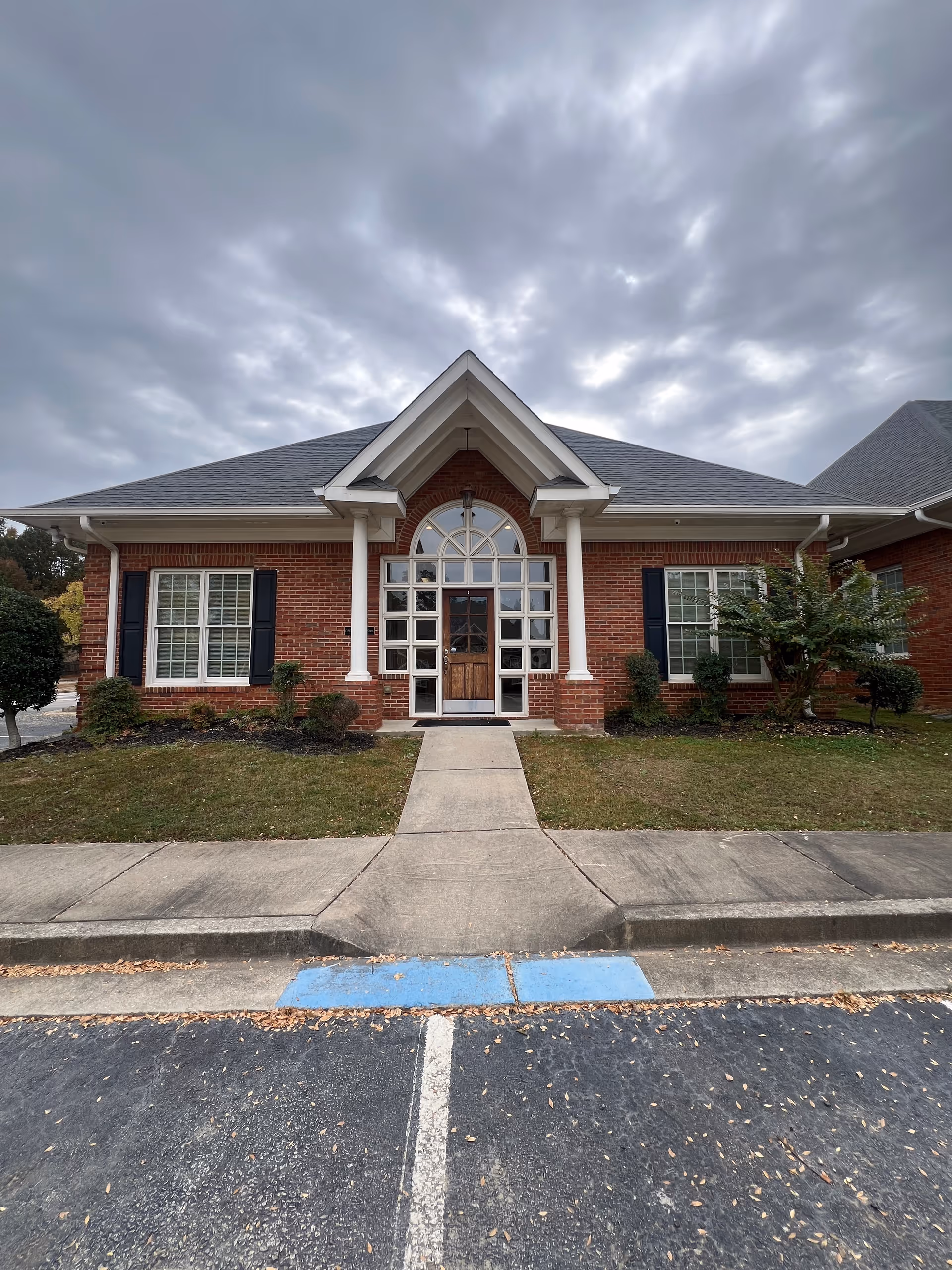 Brick senior living facility entrance with arched windows, columns, and a cloudy sky.