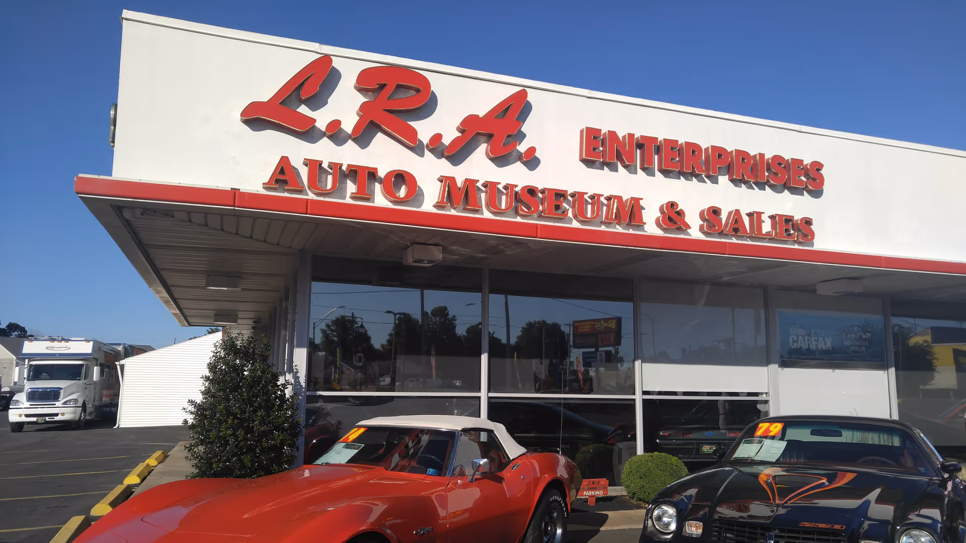 Front view of an auto museum building with red signage and vintage cars.