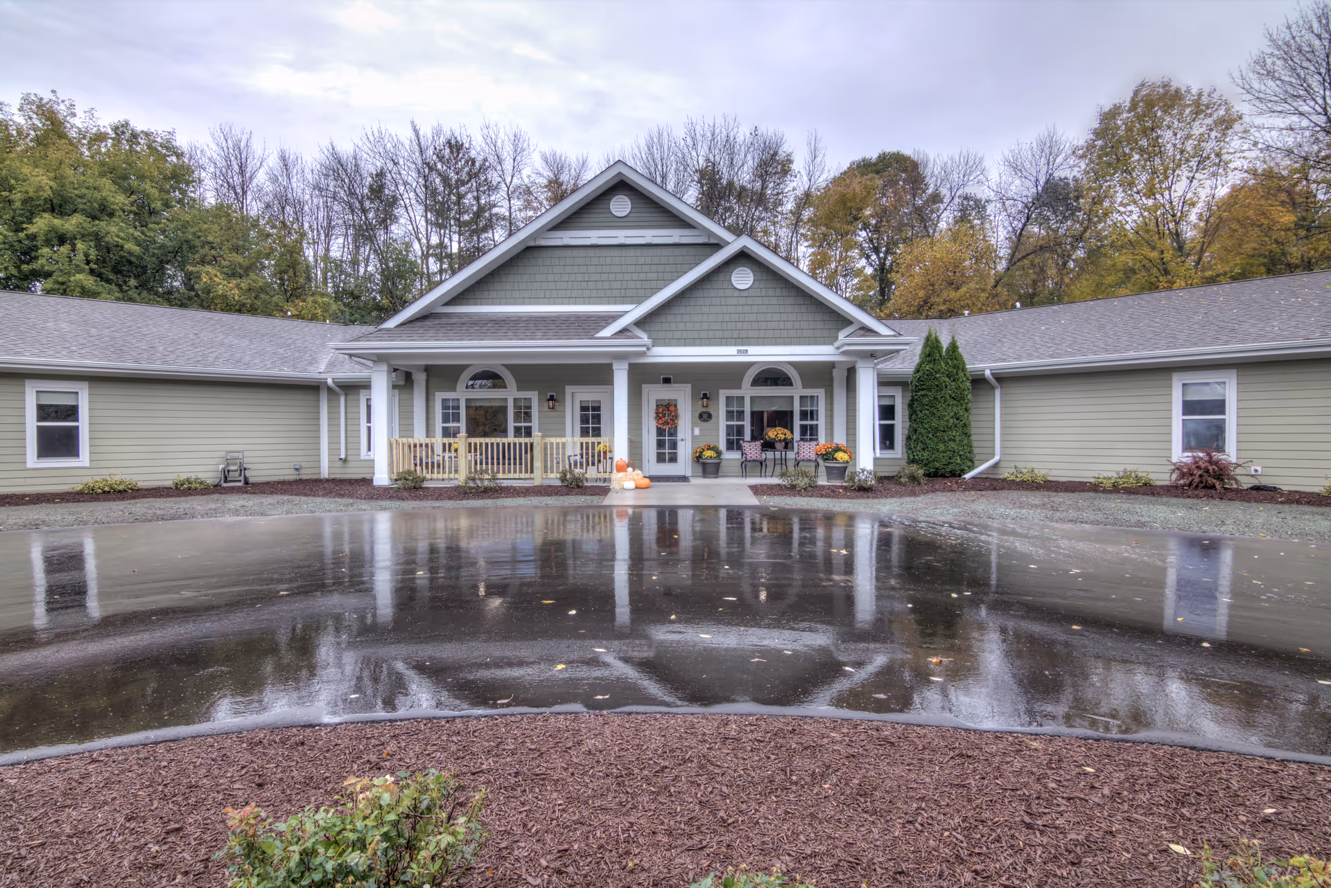 Single-story memory care facility with pale green siding and a welcoming front entrance.