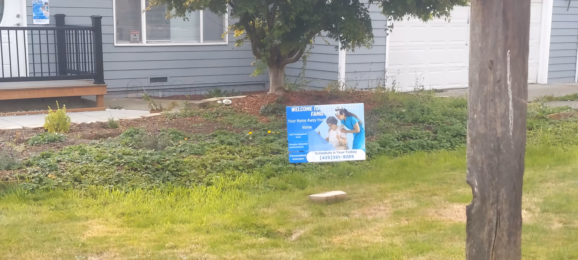 Exterior of a light blue home with a front yard sign for Westmont Adult Family Home.