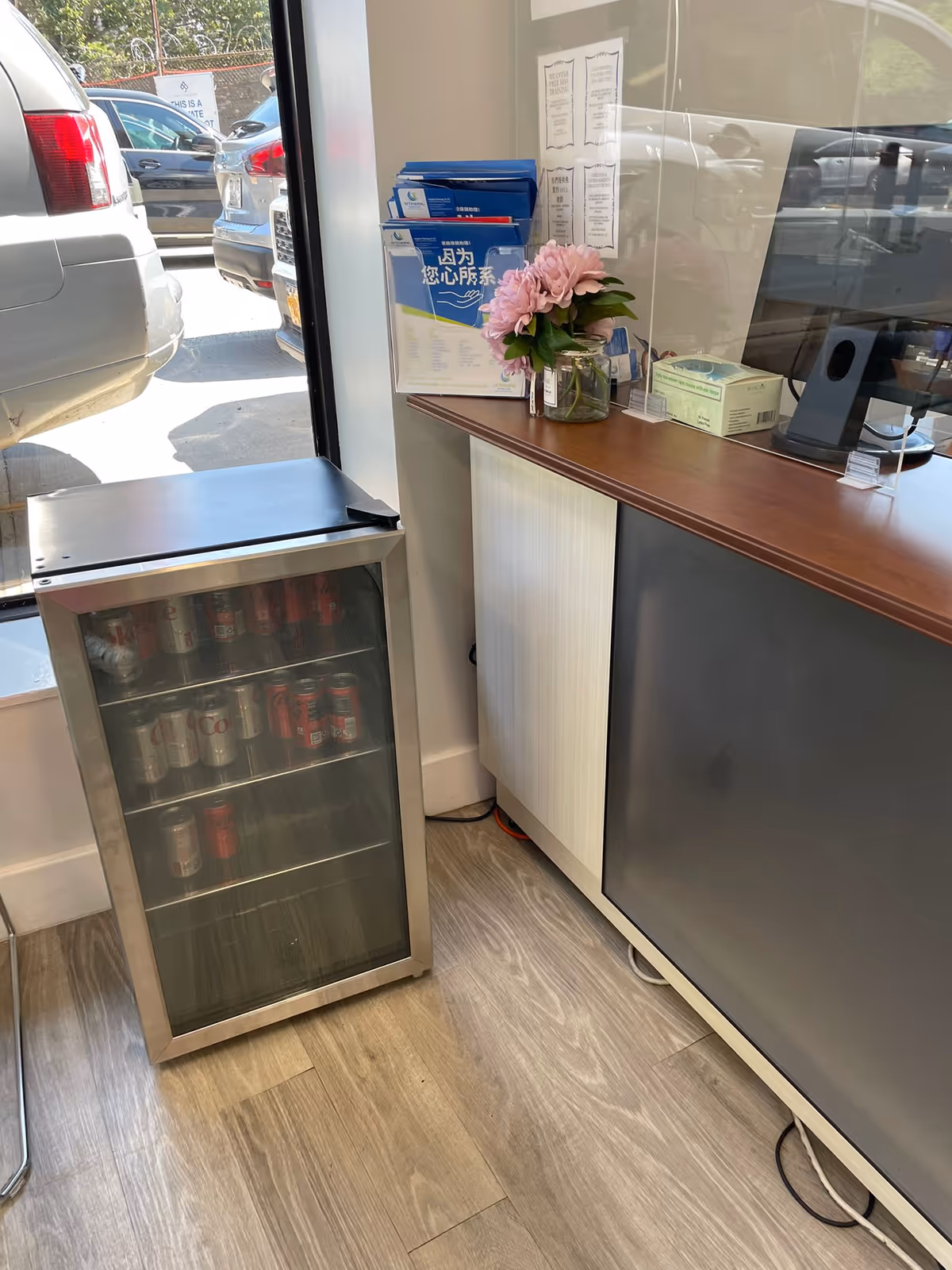 Reception area with a beverage fridge, counter, and pink flowers by the window.