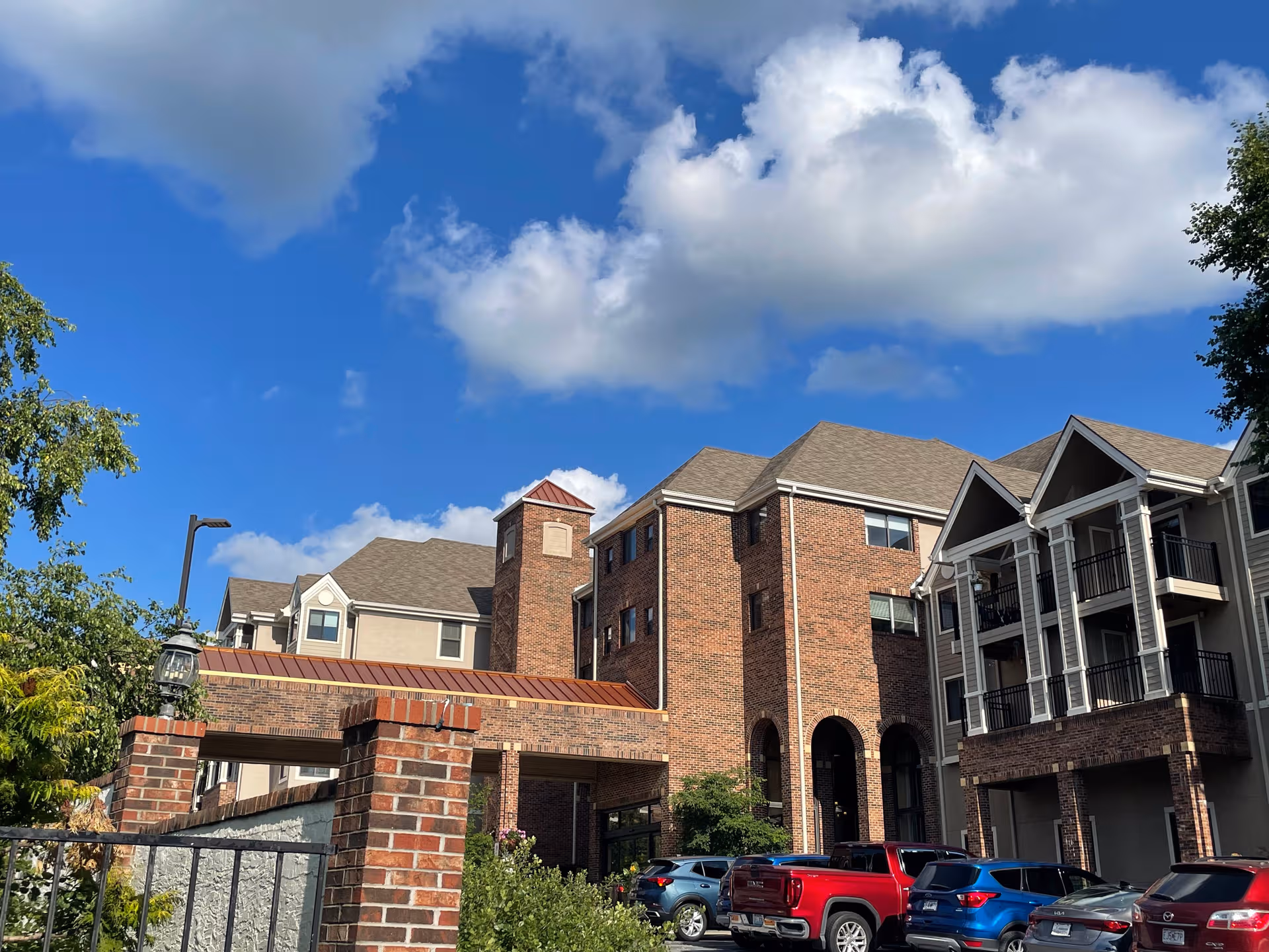 Exterior view of Brookdale Wornall Place, brick building with parked cars under a blue sky.
