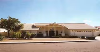 Single-story beige senior living facility with arched entrance and landscaped front.