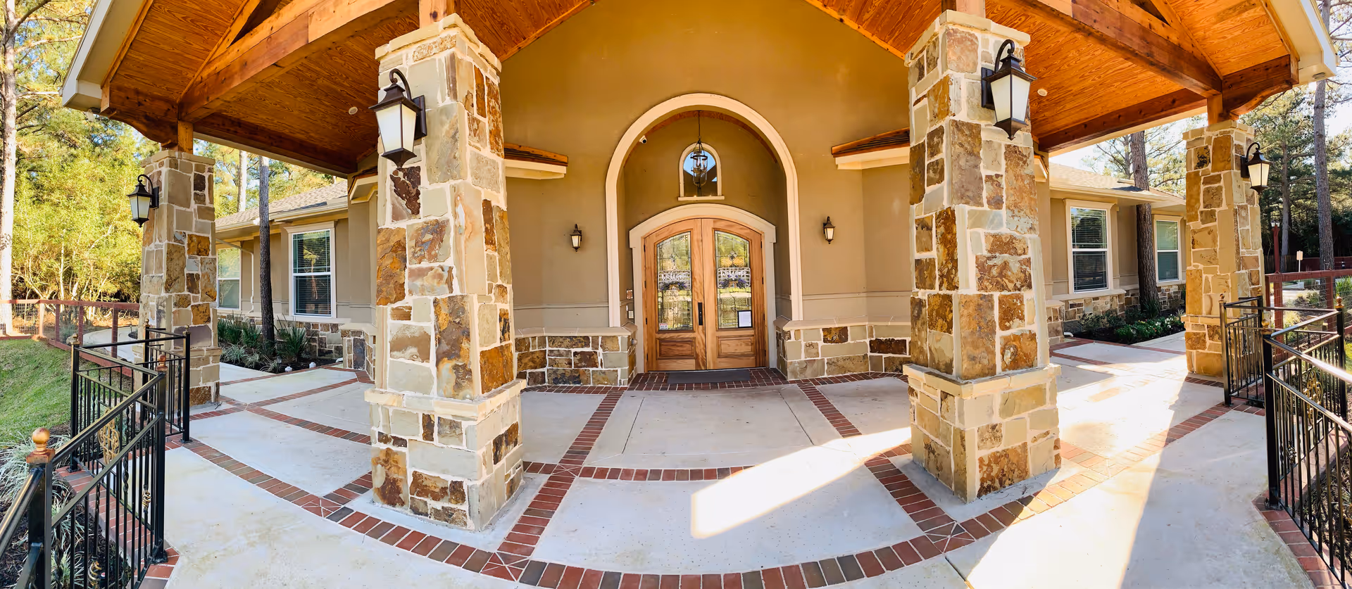 Stone columns frame a wooden arched entrance on the front porch of a senior living building.