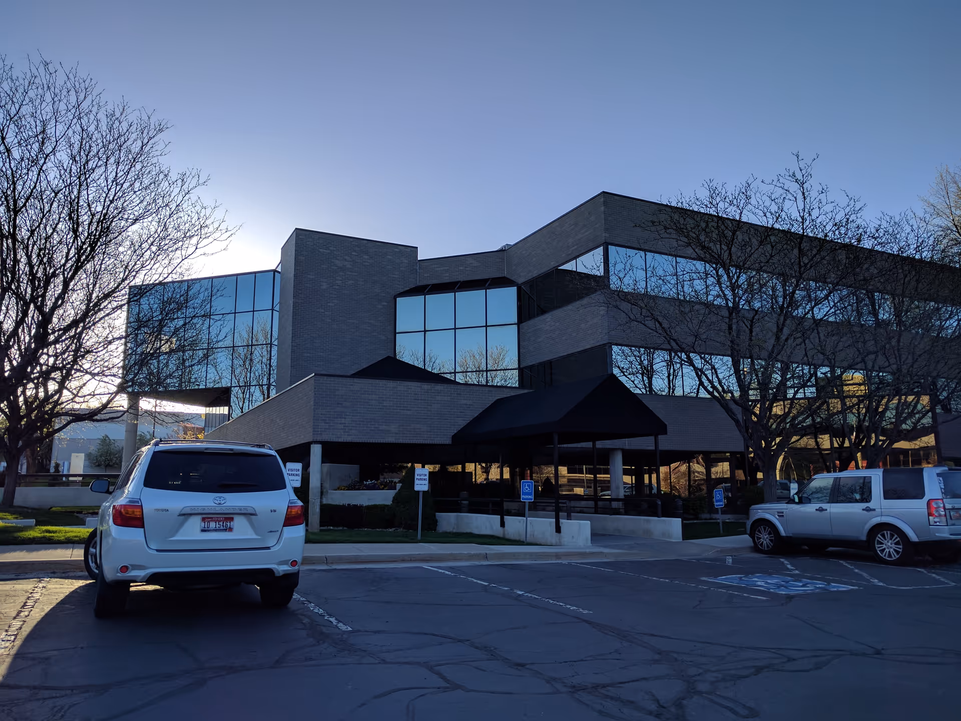 Modern senior care building with glass facade, trees, and parked cars in a front lot.
