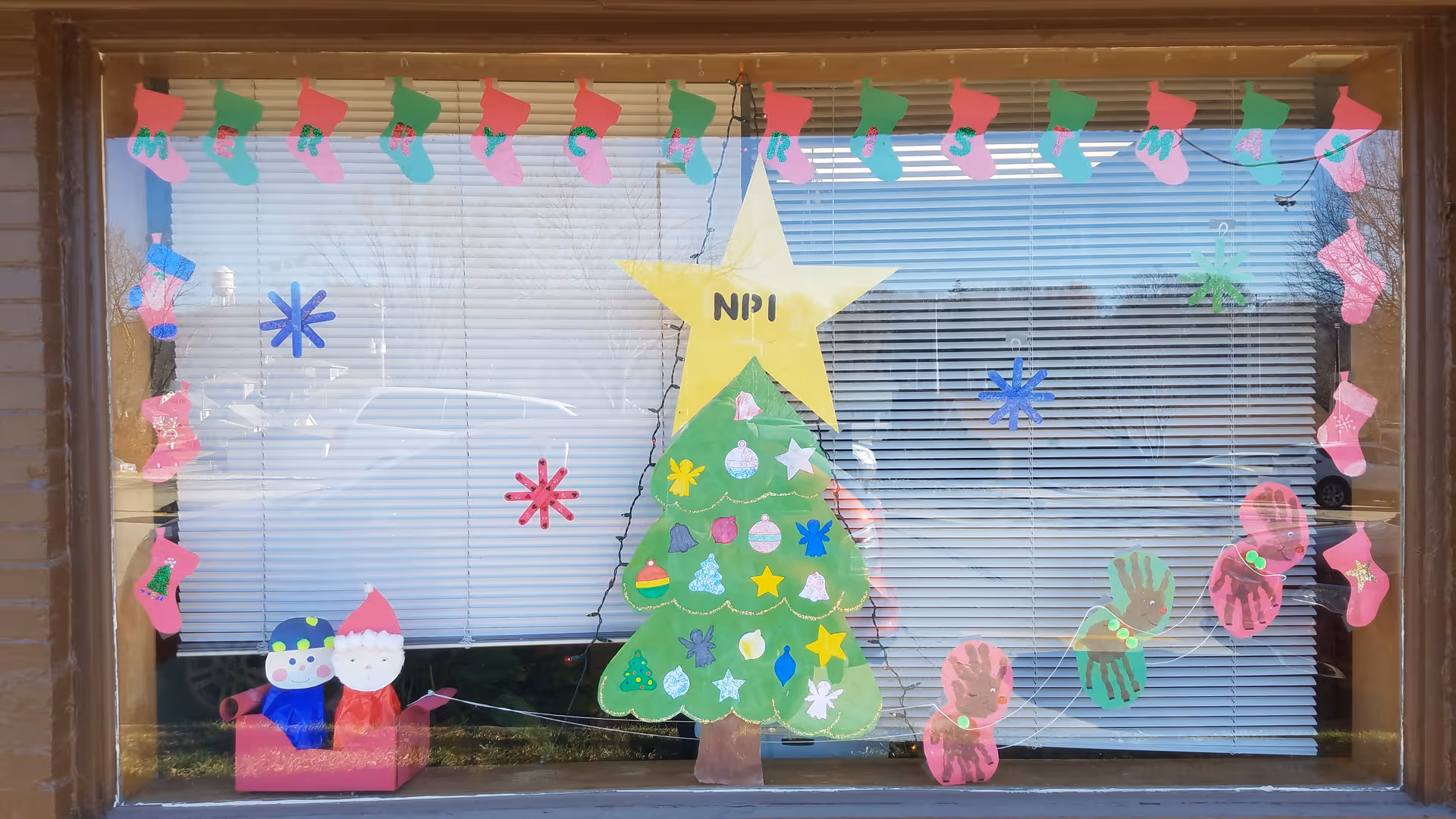 Decorated storefront window featuring a paper Christmas tree, stockings, and star decorations.