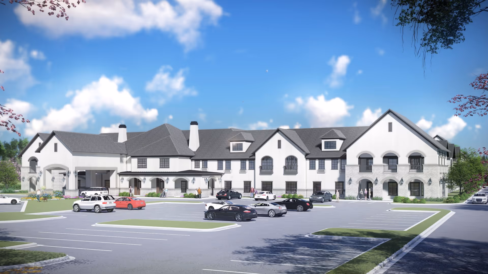 Exterior view of a large two-story senior living facility building with a gray roof and white walls, surrounded by a parking lot with several cars and a few people walking near the entrance under a partly cloudy blue sky.