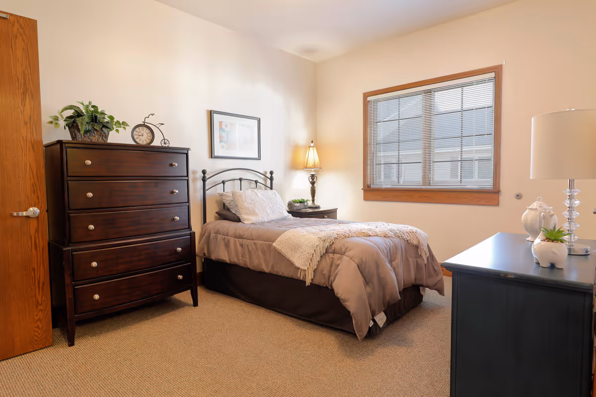 Cozy bedroom with a bed, dresser, window, and nightstand in beige tones.
