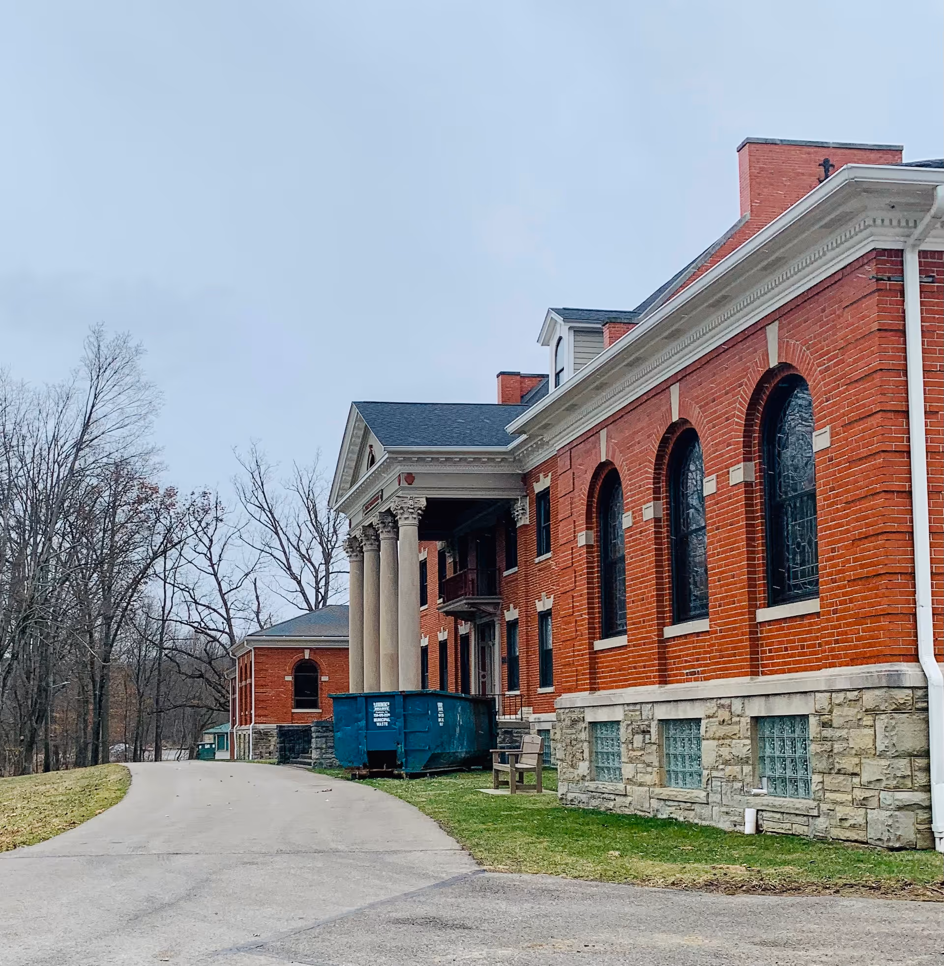 Red brick senior living building with columns and arched windows along a curved driveway.