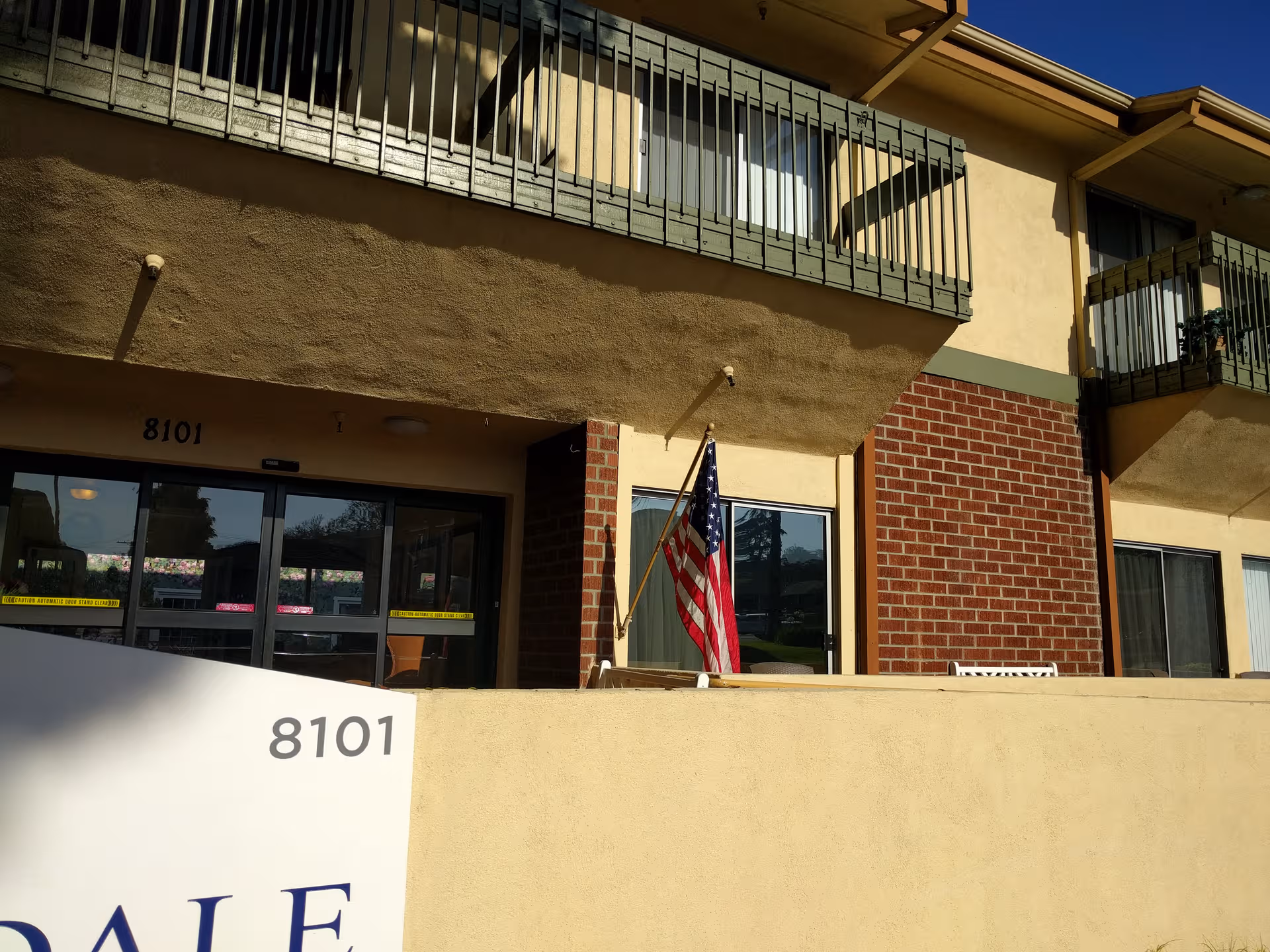 Exterior view of Brookdale Central Whittier entrance with American flag and balconies.