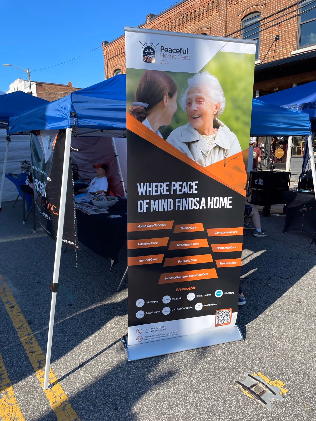 Outdoor promotional booth for Peaceful Home Care with a tall banner and blue tents.