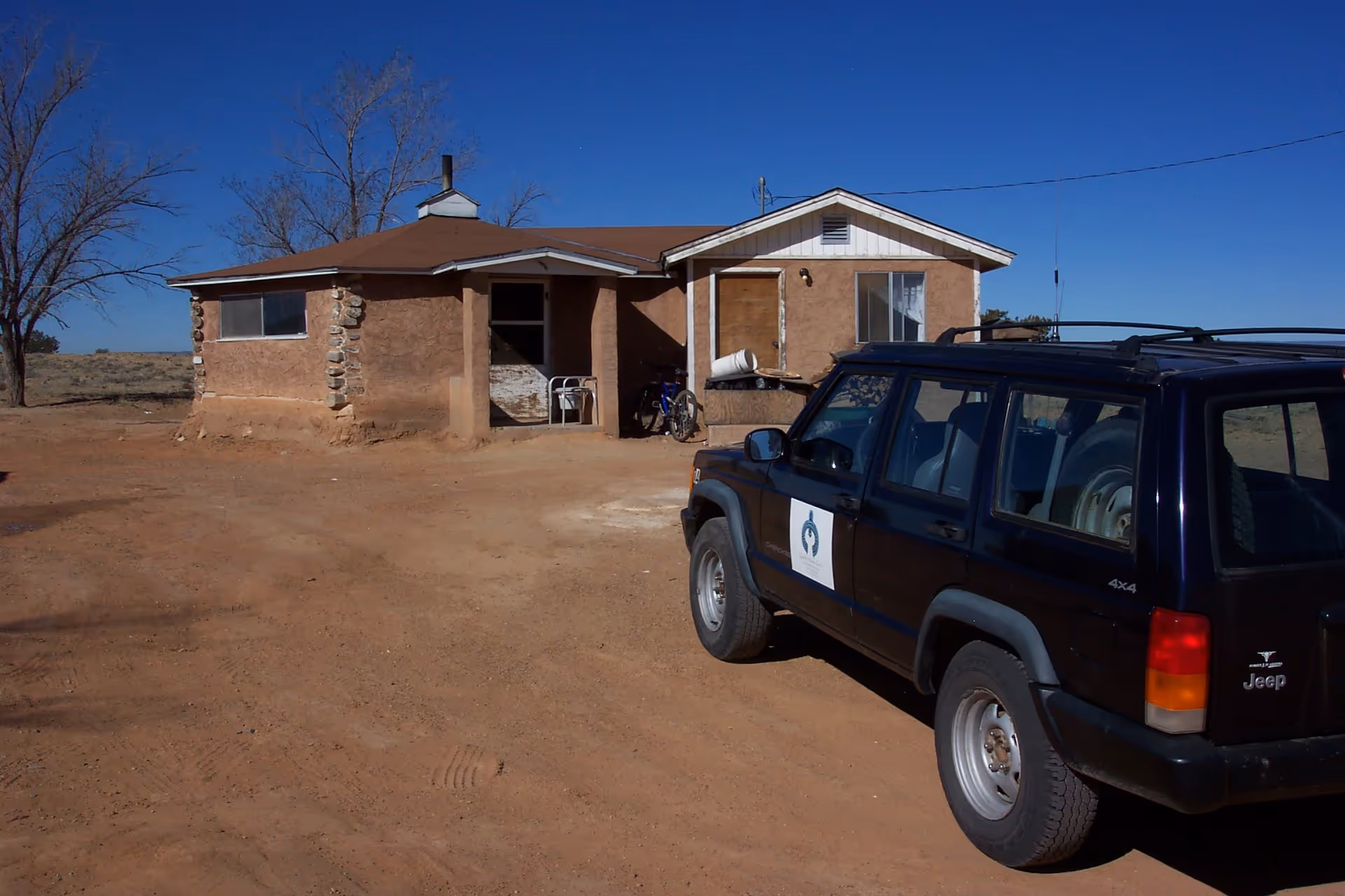 Rural single-story building with a parked dark SUV in a dusty yard.