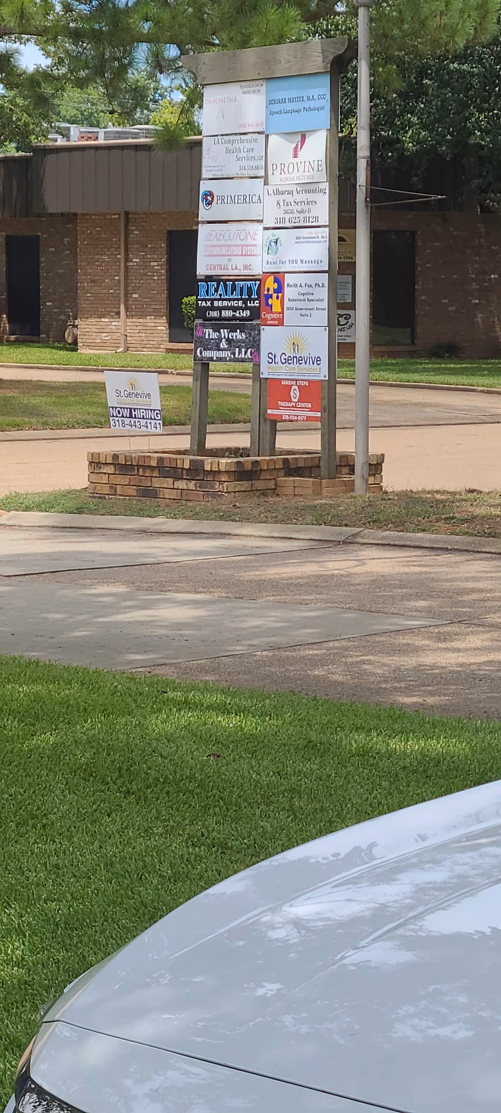 Cluster of business signs on a brick pedestal beside a parking lot, with building behind.