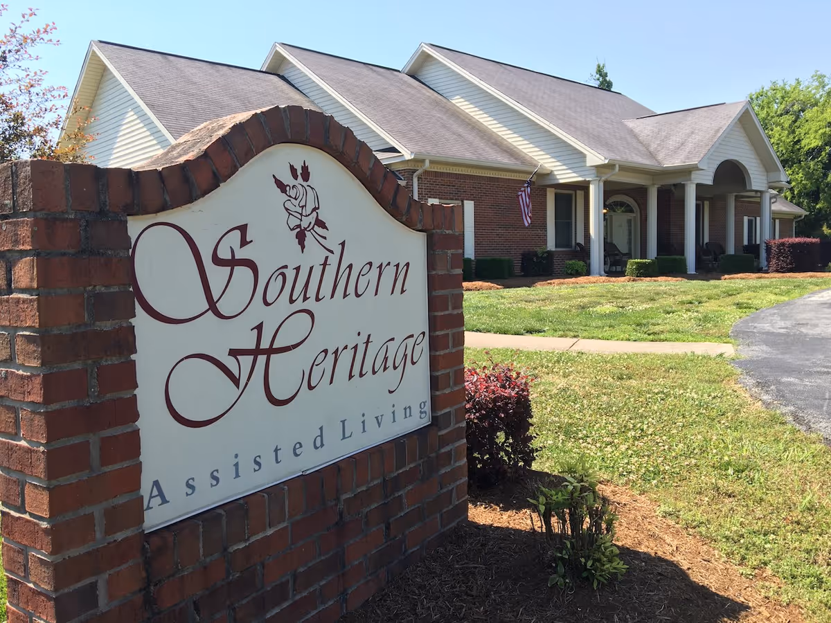 Brick sign reading "Southern Heritage Assisted Living" in front of a one-story Southern-style senior living building with columns and a lawn.